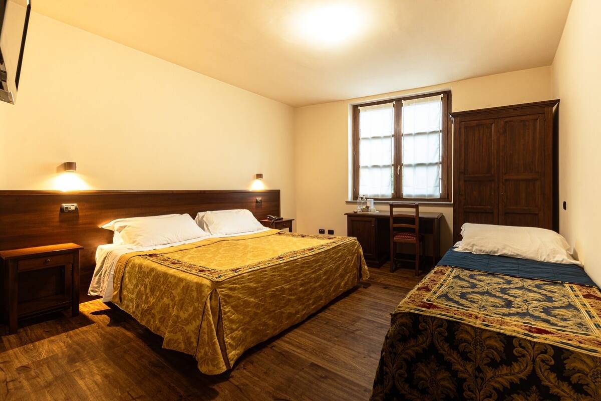 A room with two beds, wooden headboards, a desk, and a window.