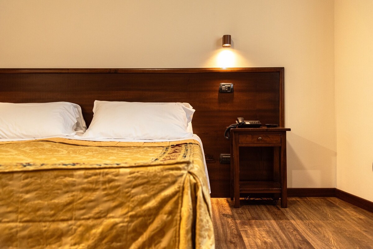 A neatly made bed with a wooden headboard, a bedside table with a lamp, and a wall-mounted light fixture.