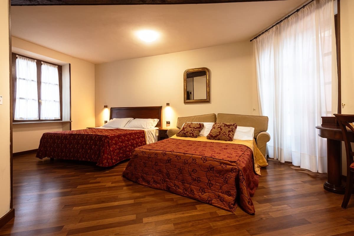 A hotel room with two beds, wooden flooring, a large window with curtains, a mirror, and a wooden nightstand.