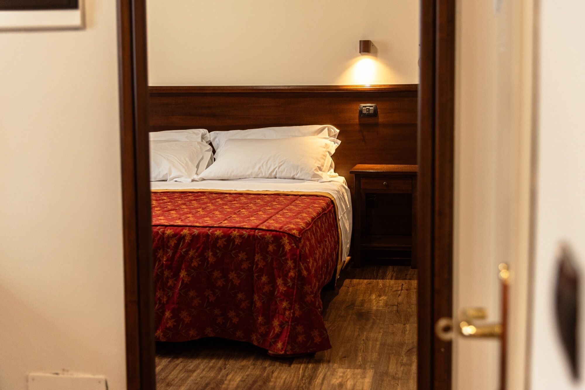 A hotel room with a bed, a nightstand, and a wall-mounted light.