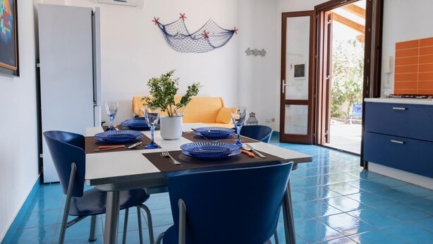 A dining area with a table set for four, blue chairs, a potted plant, and a blue and white color scheme. - Casa Orchidea Bianca with large equipped veranda (San Vito Lo Capo)