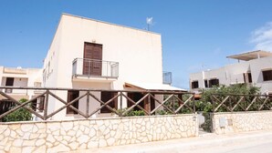 A modern two-story building with a balcony, stone wall, and a clear blue sky. - Casa Orchidea Bianca with large equipped veranda (San Vito Lo Capo)