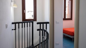 Ein Flur, der in ein Schlafzimmer mit Fenster, Tür und Leuchte führt.
