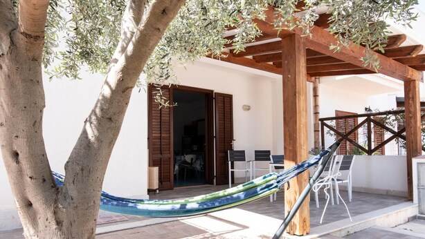Eine Hängematte unter einer Holzpergola, ein Sitzbereich im Freien und der Eingang eines Gebäudes mit einer Tür.
