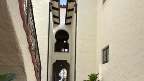 Un étroit sentier pavé, bordé de murs blancs aux encadrements sombres et surmonté d’un toit recouvert de tuiles.