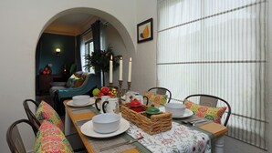 Un coin repas avec une table dressée pour quatre personnes, agrémenté d’une nappe à motifs floraux, d’assiettes blanches et d’un panier de fruits.