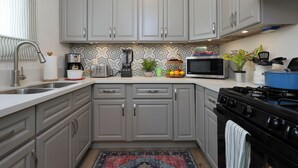 Une cuisine avec des meubles de couleur grise, un four à micro-ondes, une cuisinière et un crédence décorée.