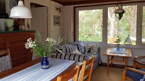 Indbydende hytteinteriør med spisebord, stole, sofa og et vindue med udsigt til træer.