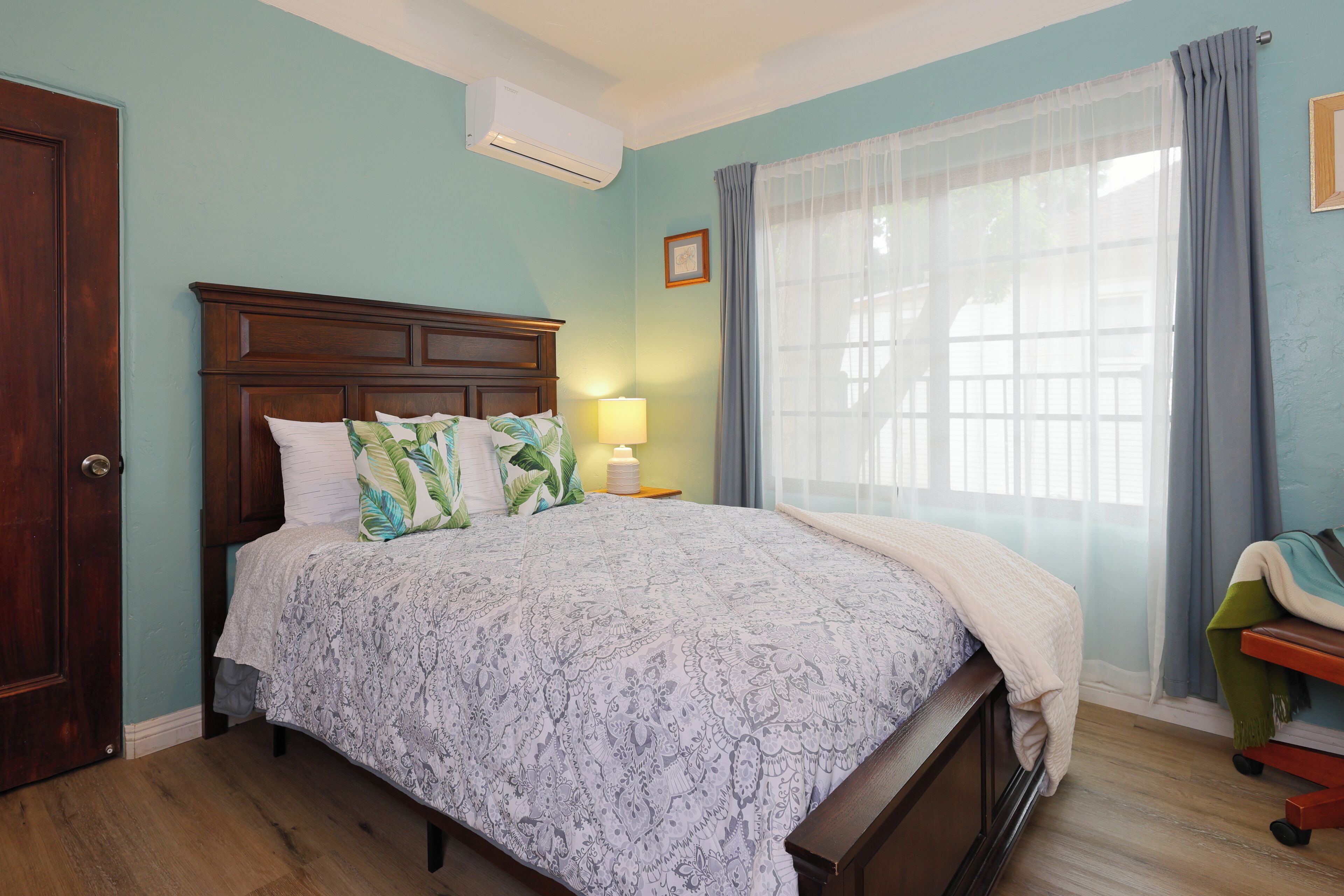 Una camera da letto con una testiera in legno, un letto con biancheria a motivi, una lampada da comodino e una finestra con tende.