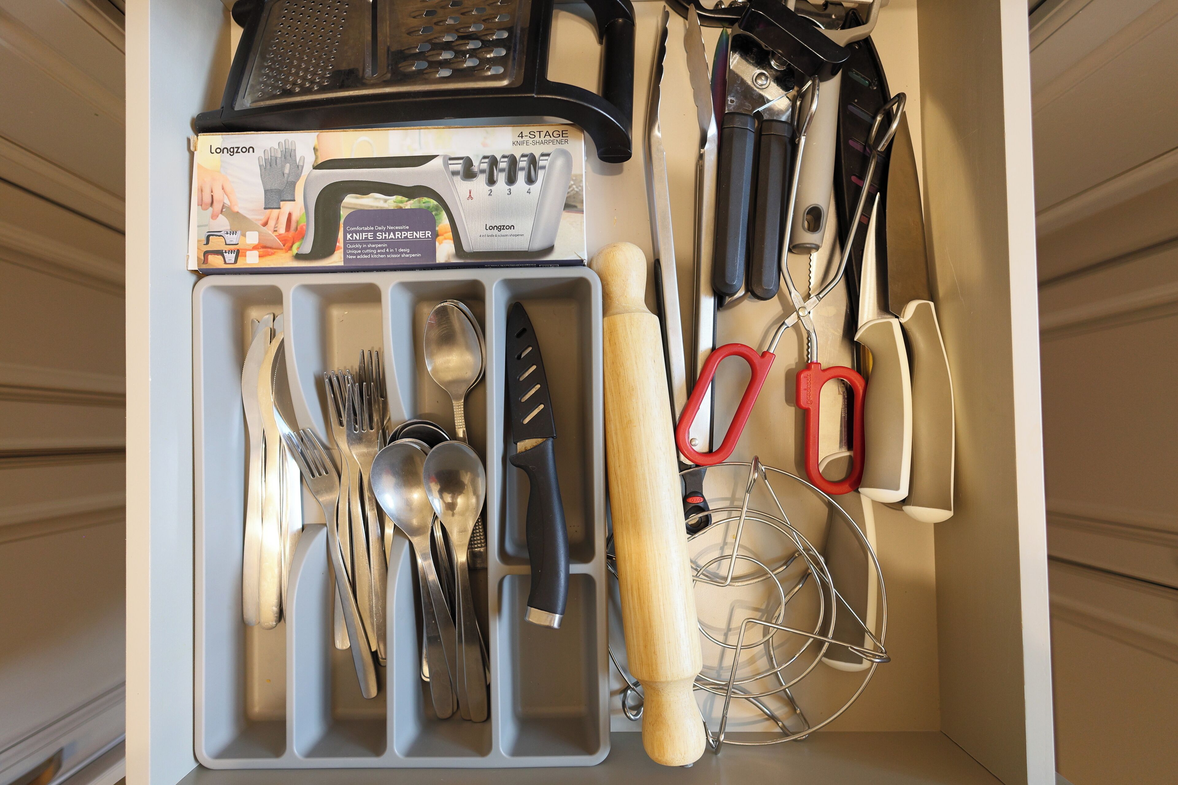 A kitchen drawer with utensils and a knife sharpener.
