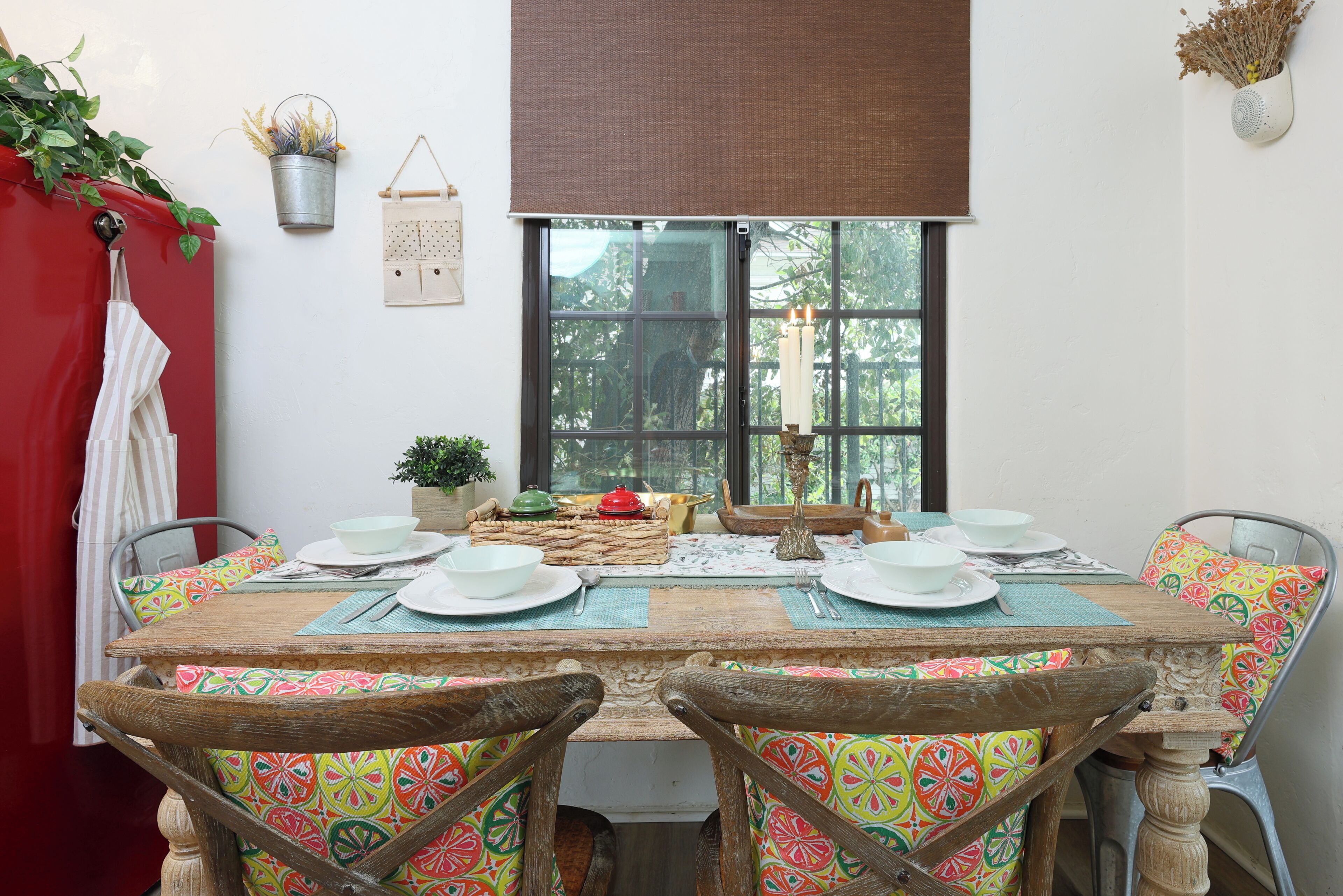 Une table à manger dressée avec des assiettes, des bols et des couverts, entourée de chaises agrémentées de coussins colorés.