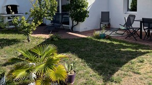 Een wit huis met blauwe luiken, een schoorsteen en een kleine tuin met palmboompjes en een rotstuin.