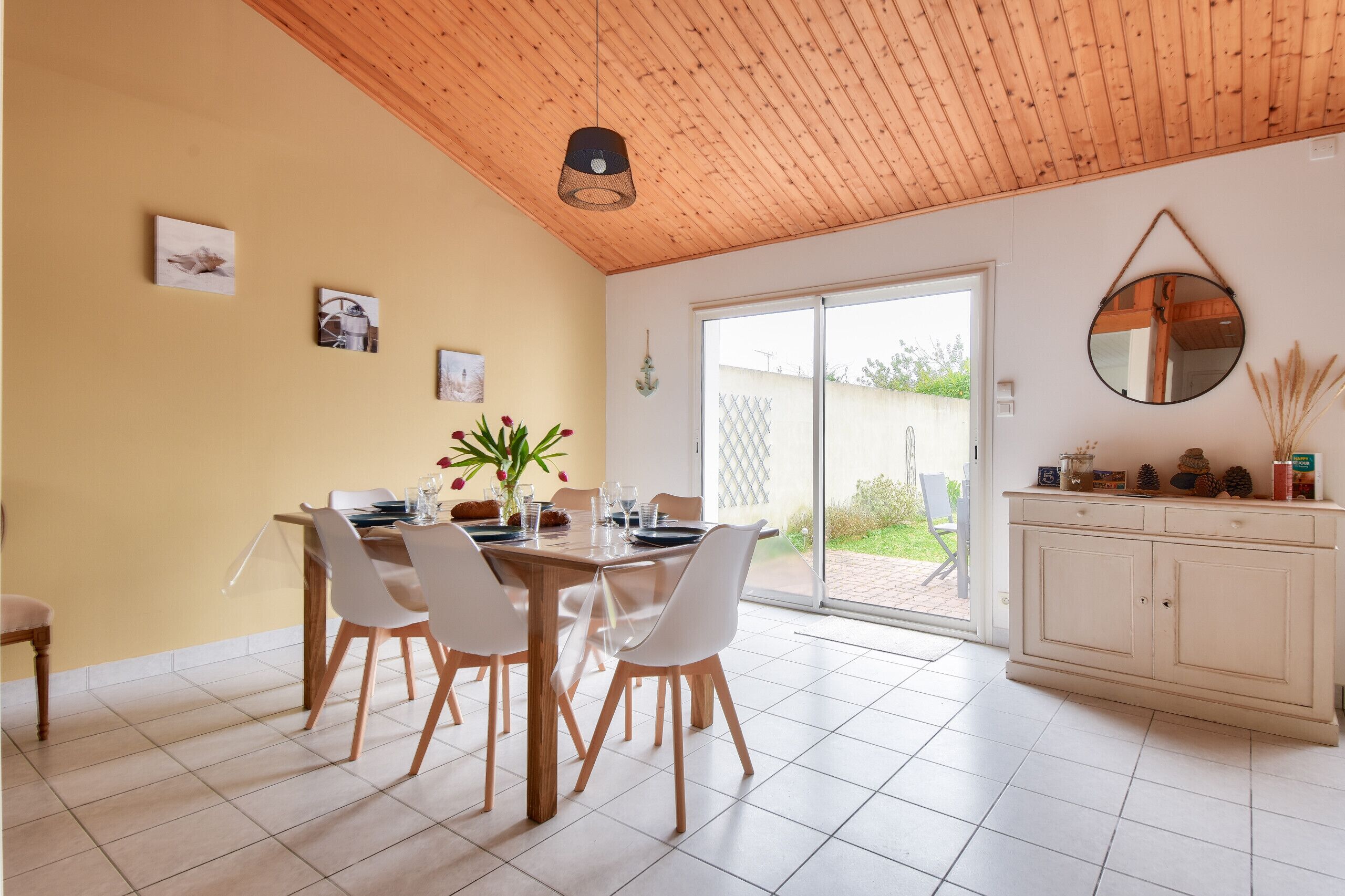 A dining area with a wooden ceiling, white chairs, a table set for four, and a sliding glass door leading to an outdoor area.