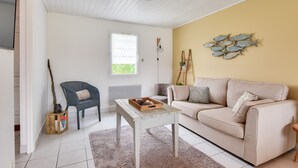 Een woonkamer met een beige bank, een witte salontafel, een rieten stoel en een decoratief kunstwerk van vissen op de muur.