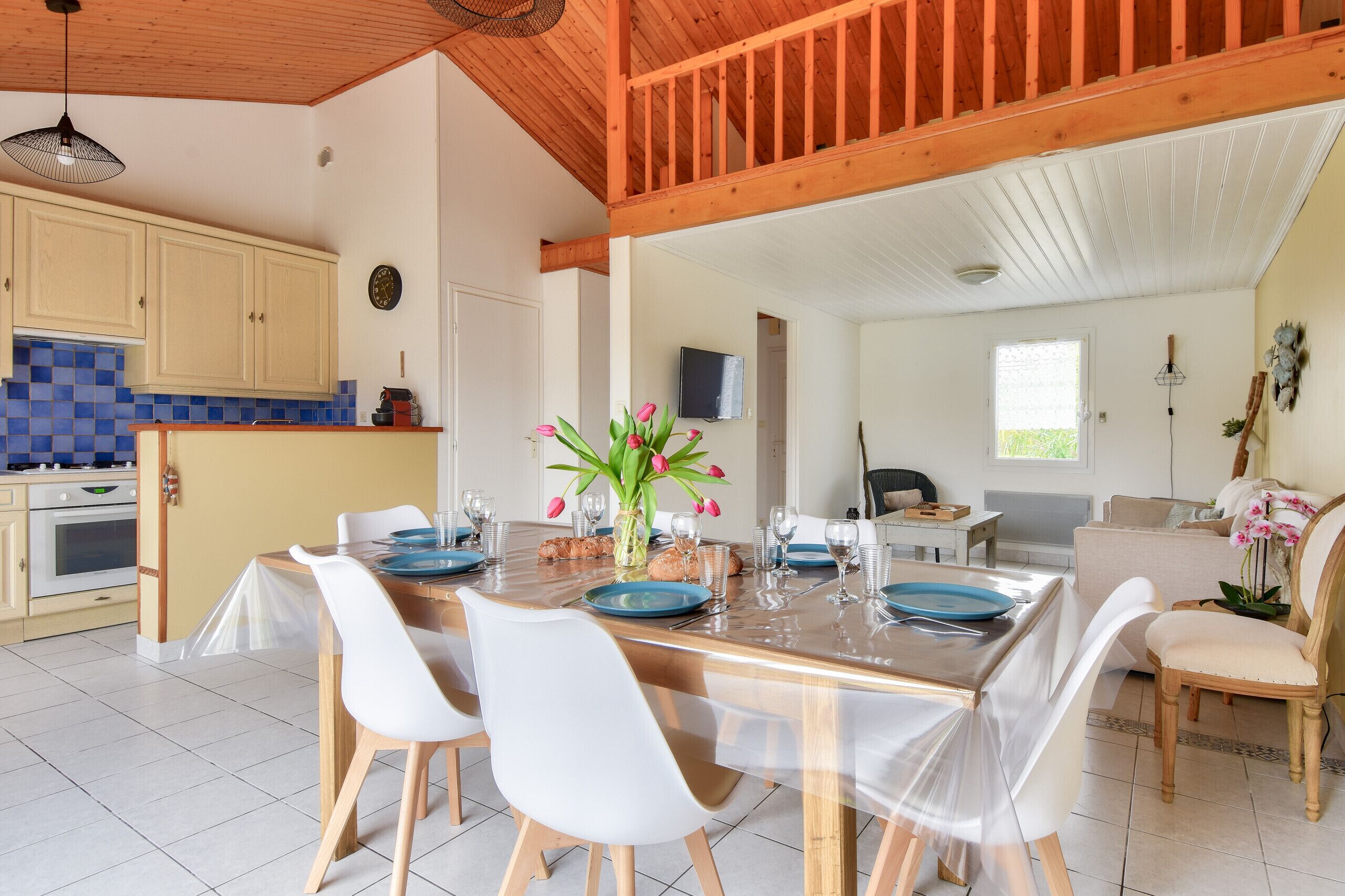 A dining area with a wooden table set for six, white chairs, and a vase with pink flowers.