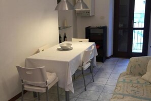 Un coin repas avec une table dressée pour deux personnes, un canapé et un espace cuisine visible au fond.
