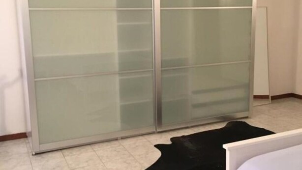 Una stanza con una porta-vetro scorrevole, un tappeto in pelle nera e una struttura letto bianca.