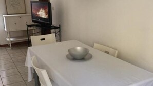 Zona pranzo con tavolo apparecchiato per due, televisore su un mobile e un armadietto bianco sullo sfondo.