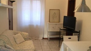 Una stanza accogliente e piccola con un divano, una TV su un mobile, un tavolo e un armadietto.