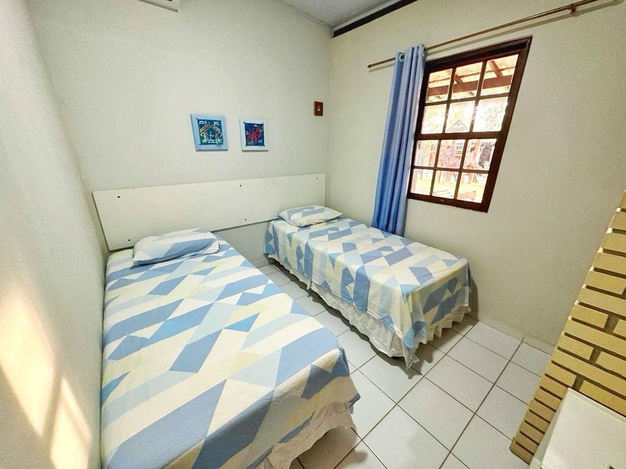 A small, clean room with two single beds, a window with curtains, and two small wall art pieces.