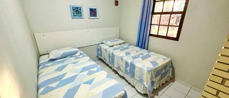 A small, clean room with two single beds, a window with curtains, and two small wall art pieces.