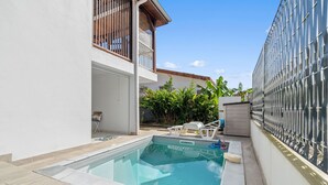 Une piscine à l’eau d’un bleu limpide, entourée d’un mur blanc et d’une clôture en métal.