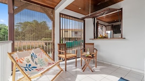Un balcon avec des chaises en bois, une petite table et une chaise agrémentée d’un coussin coloré.
