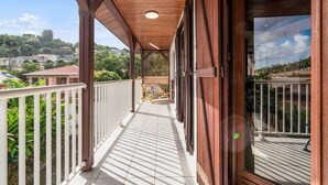 Un balcon couvert donnant sur un quartier résidentiel, avec des balustrades en bois et un sol carrelé.