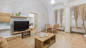 A modern living room with a brick wall, wooden furniture, a flat-screen TV, and a dining area with a table and chairs. - Venus Apartments - Oktogon I (Budapest)