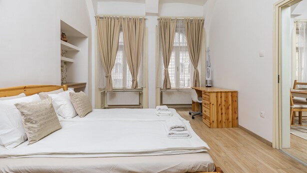A bedroom with a large bed, two windows with curtains, a wooden desk, and a radiator. - Venus Apartments - Oktogon I (Budapest)