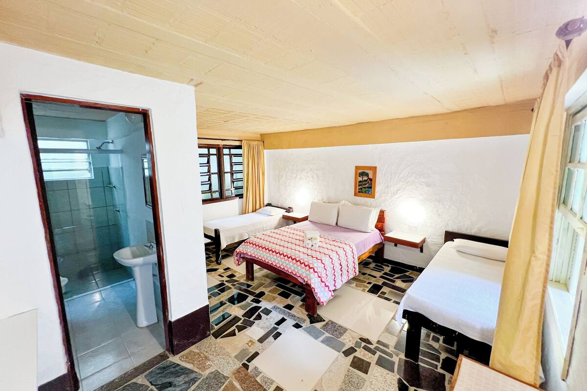 A hotel room with a tiled floor, a bed with a red and white striped bedspread, a bedside table, and a window with curtains.