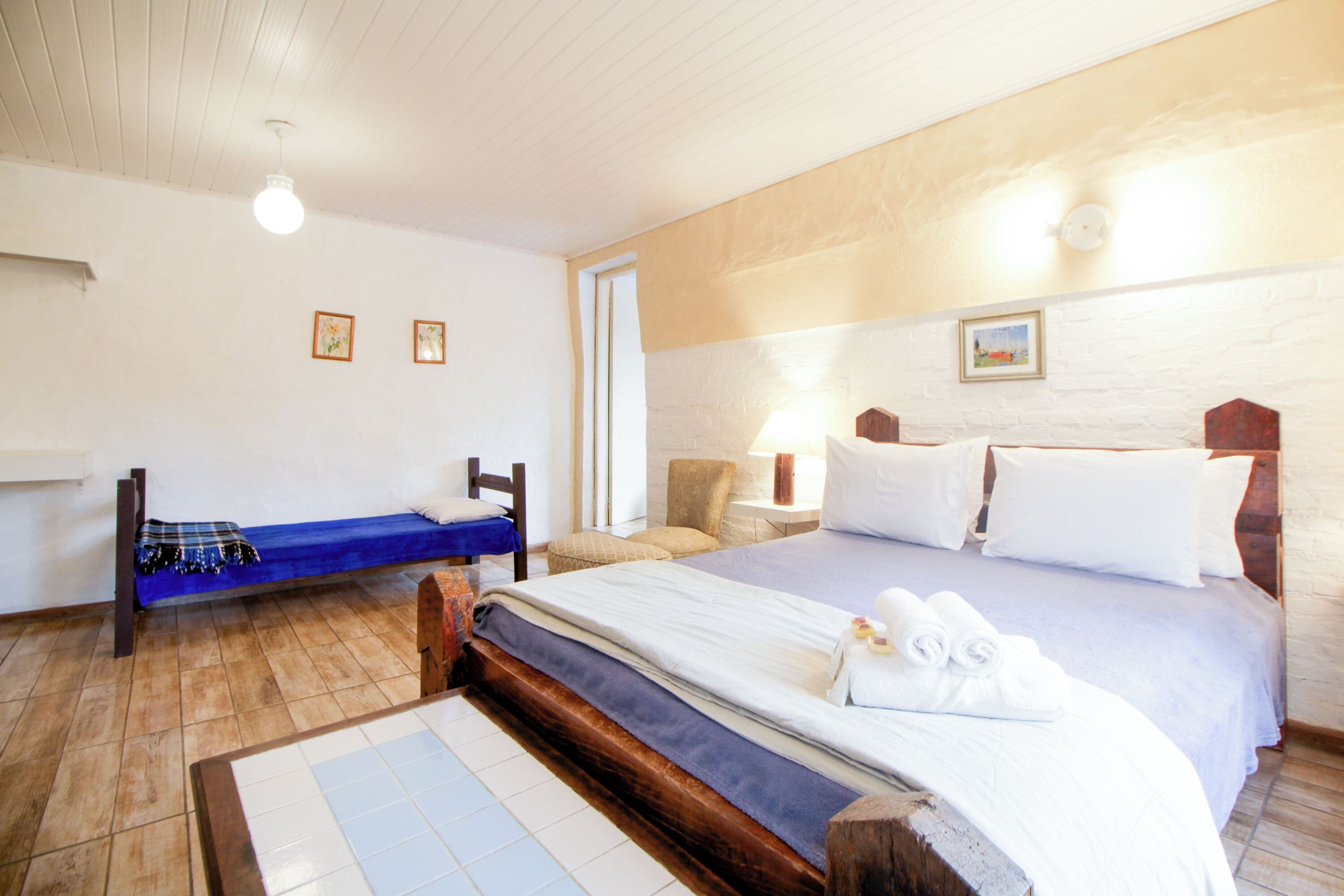 Een slaapkamer met een groot bed, een kleiner bed, een bankje en een houten tafel.