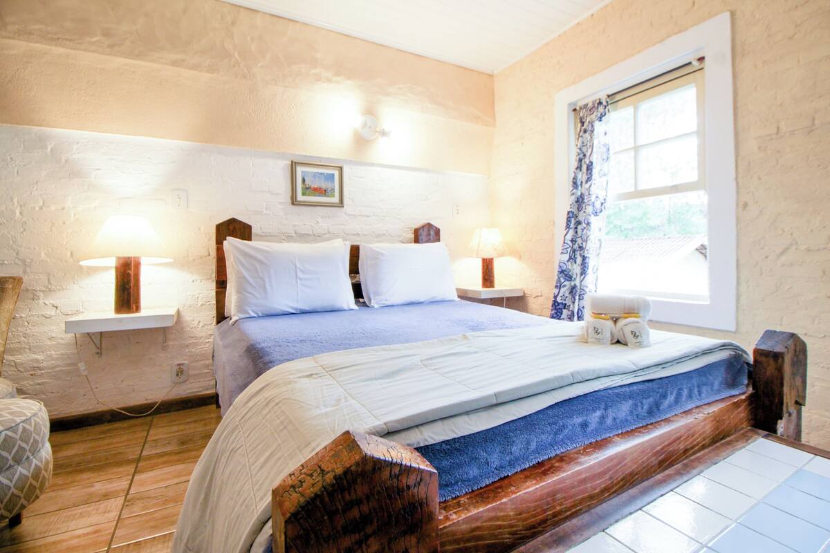 A bedroom with a wooden bed, white walls, a window with a curtain, and two bedside lamps.