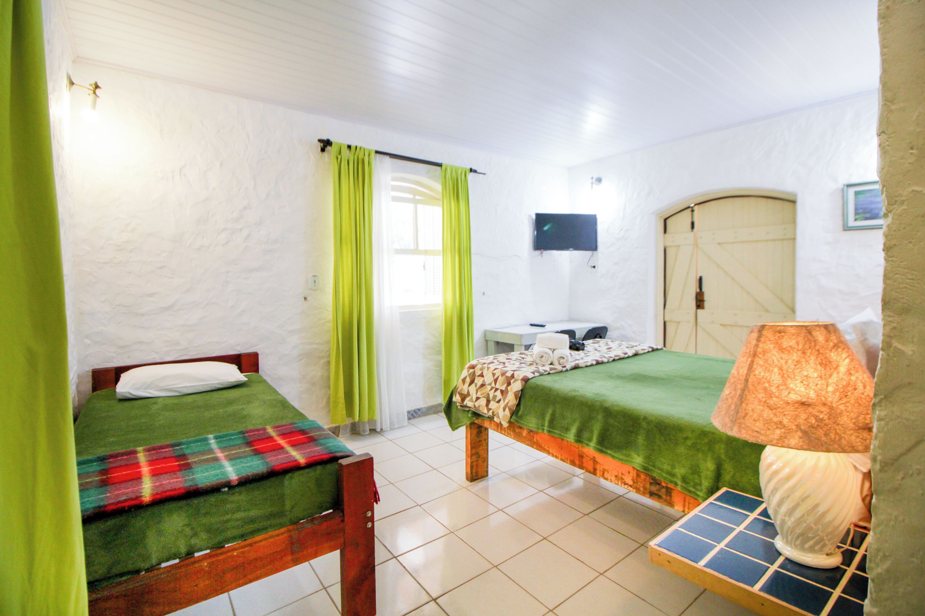 A room with two beds, a television, a door, and a window with curtains.