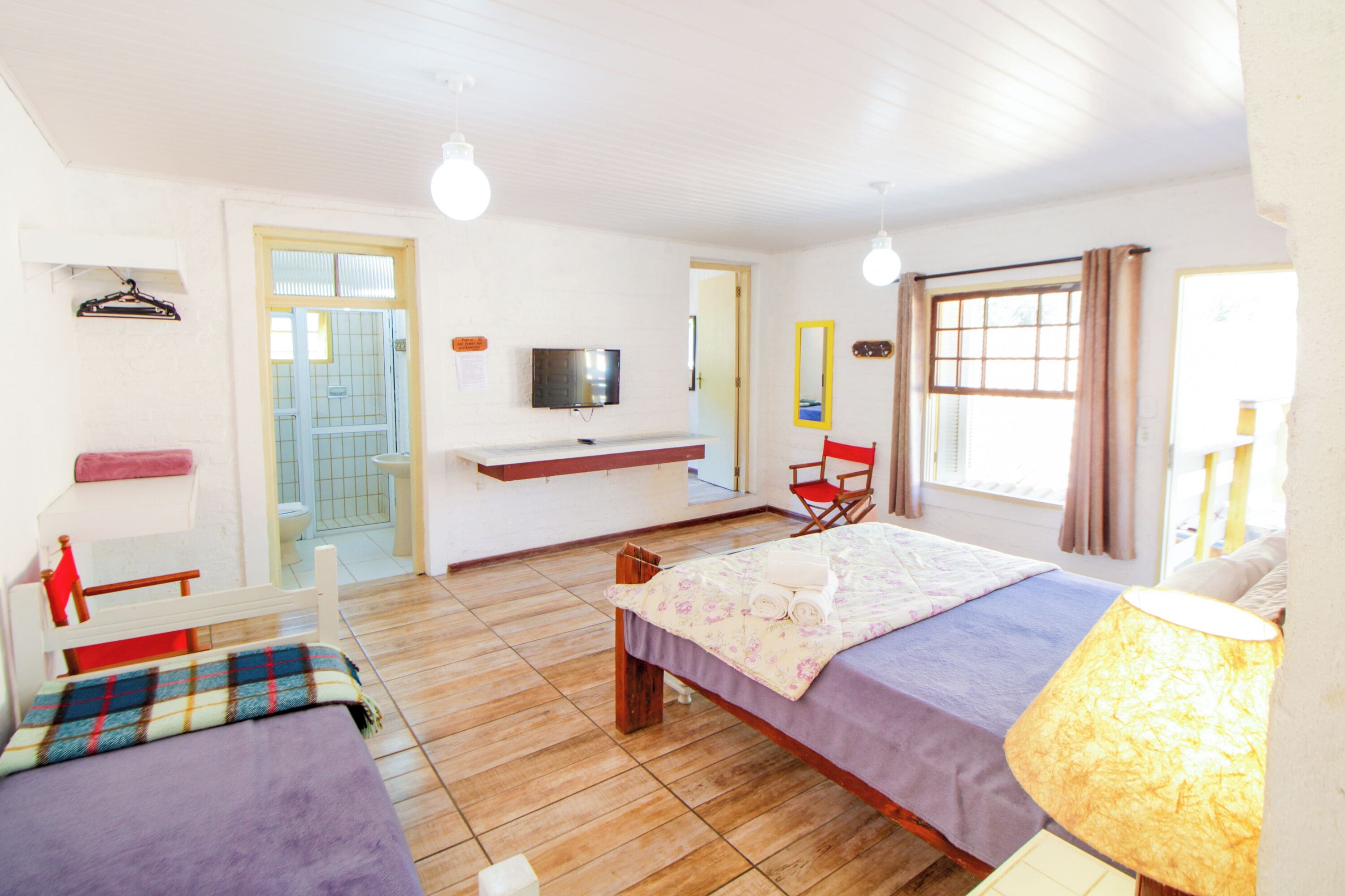 A bedroom with a bed, a chair, a TV, and a window.