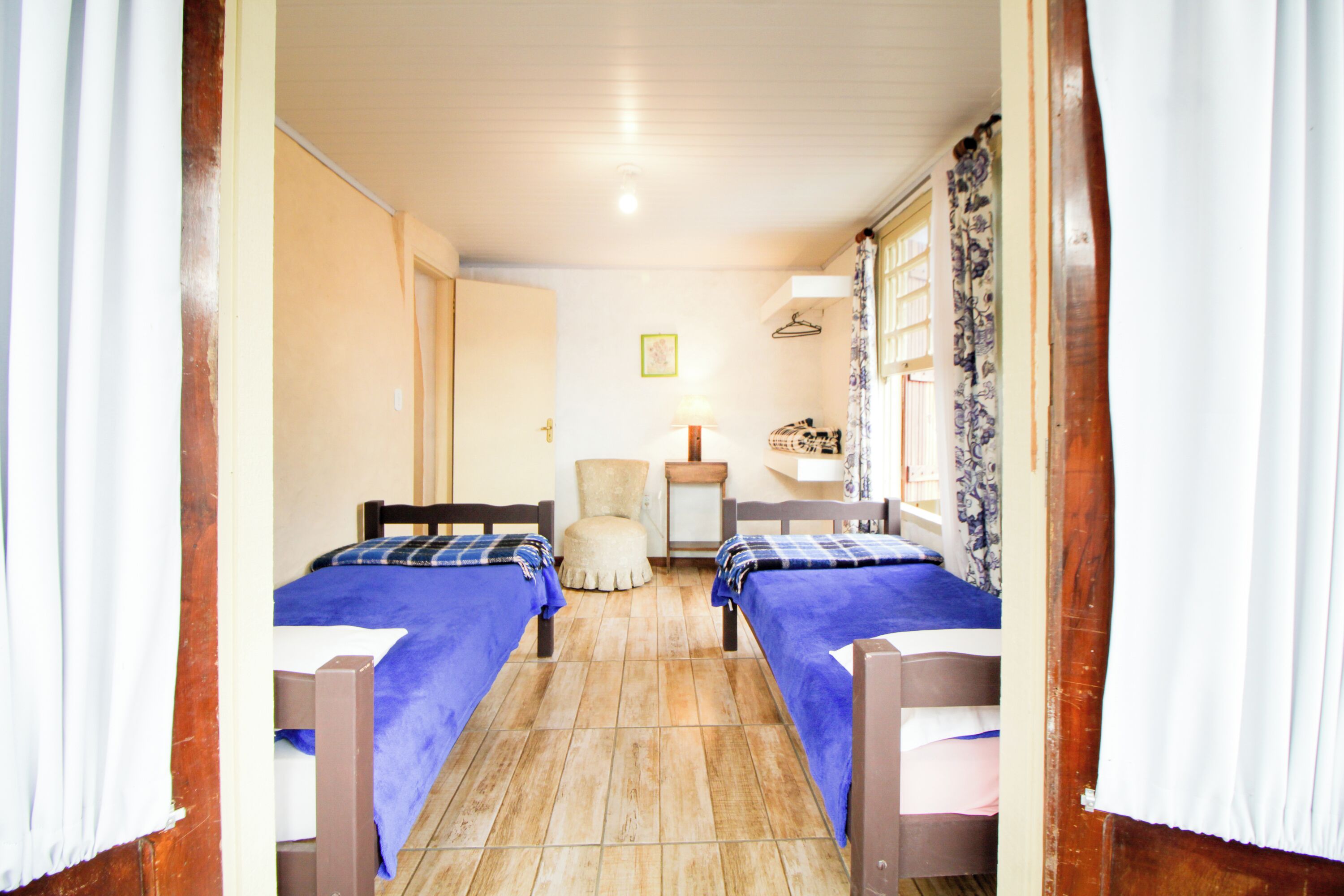 A room with two beds, a chair, a small table, and a window with curtains.