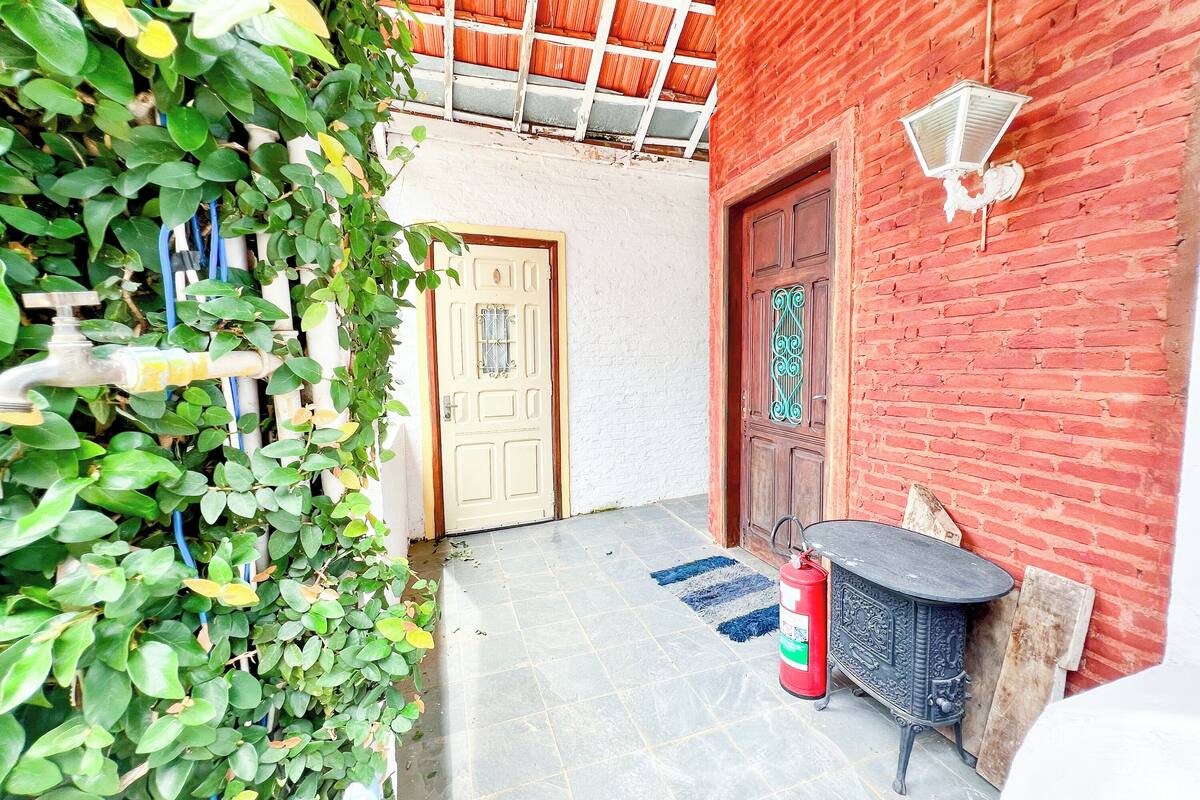 A narrow outdoor corridor with a tiled floor, a wooden door, a red brick wall, and a metal table with a fire extinguisher.