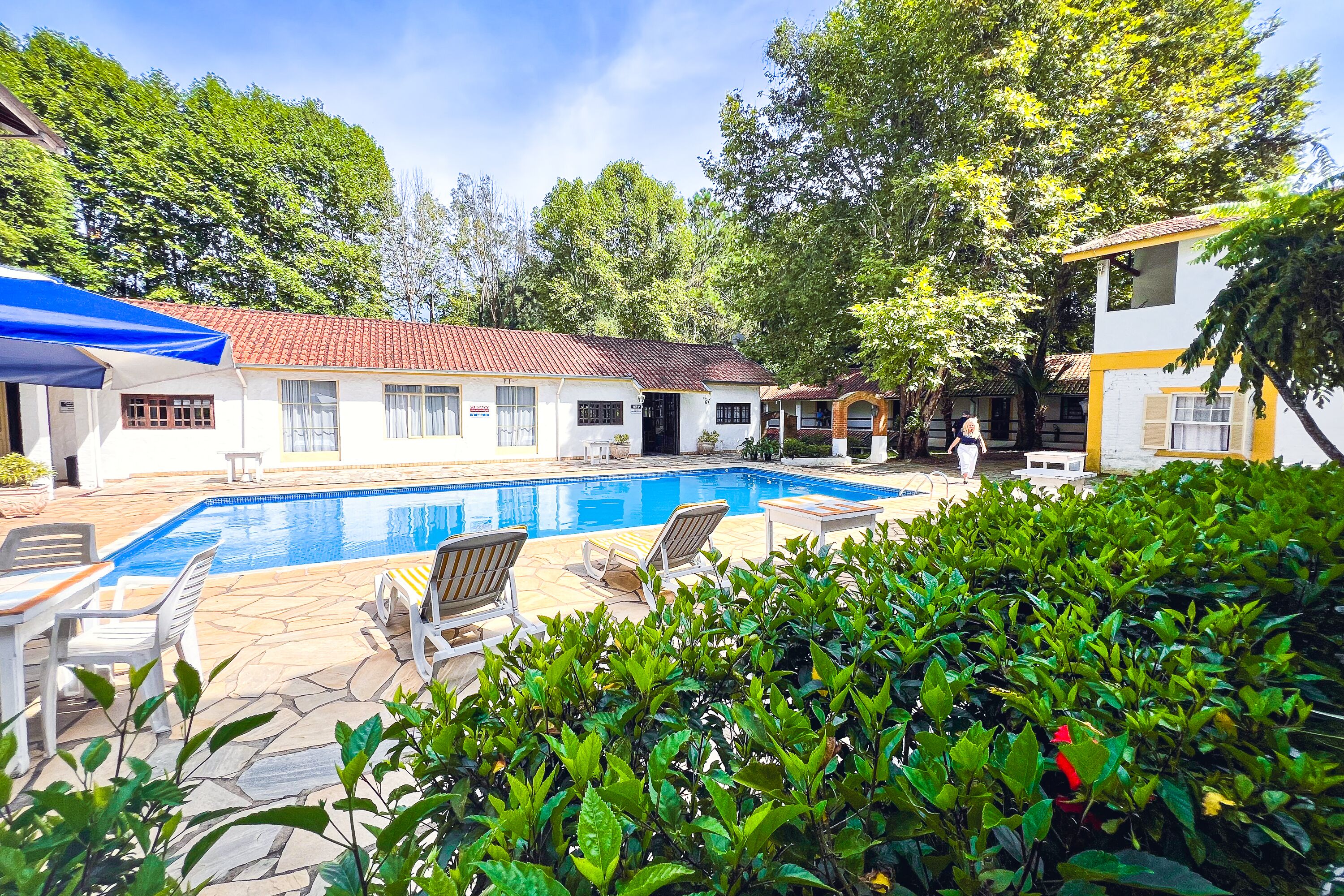 Uma piscina com espreguiçadeiras, um alpendre coberto e um edifício com telhado em azulejos.