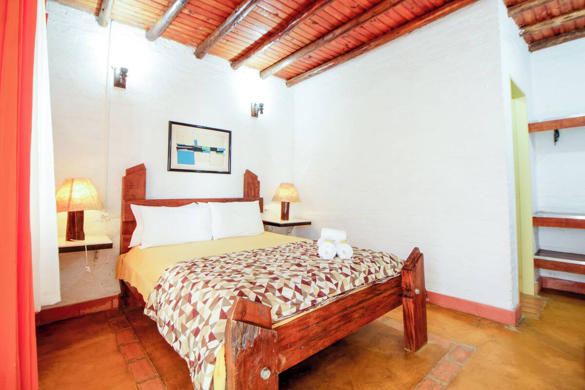 A single bed with a geometric patterned bedspread, two bedside lamps, a framed picture on the wall, and a wooden headboard.