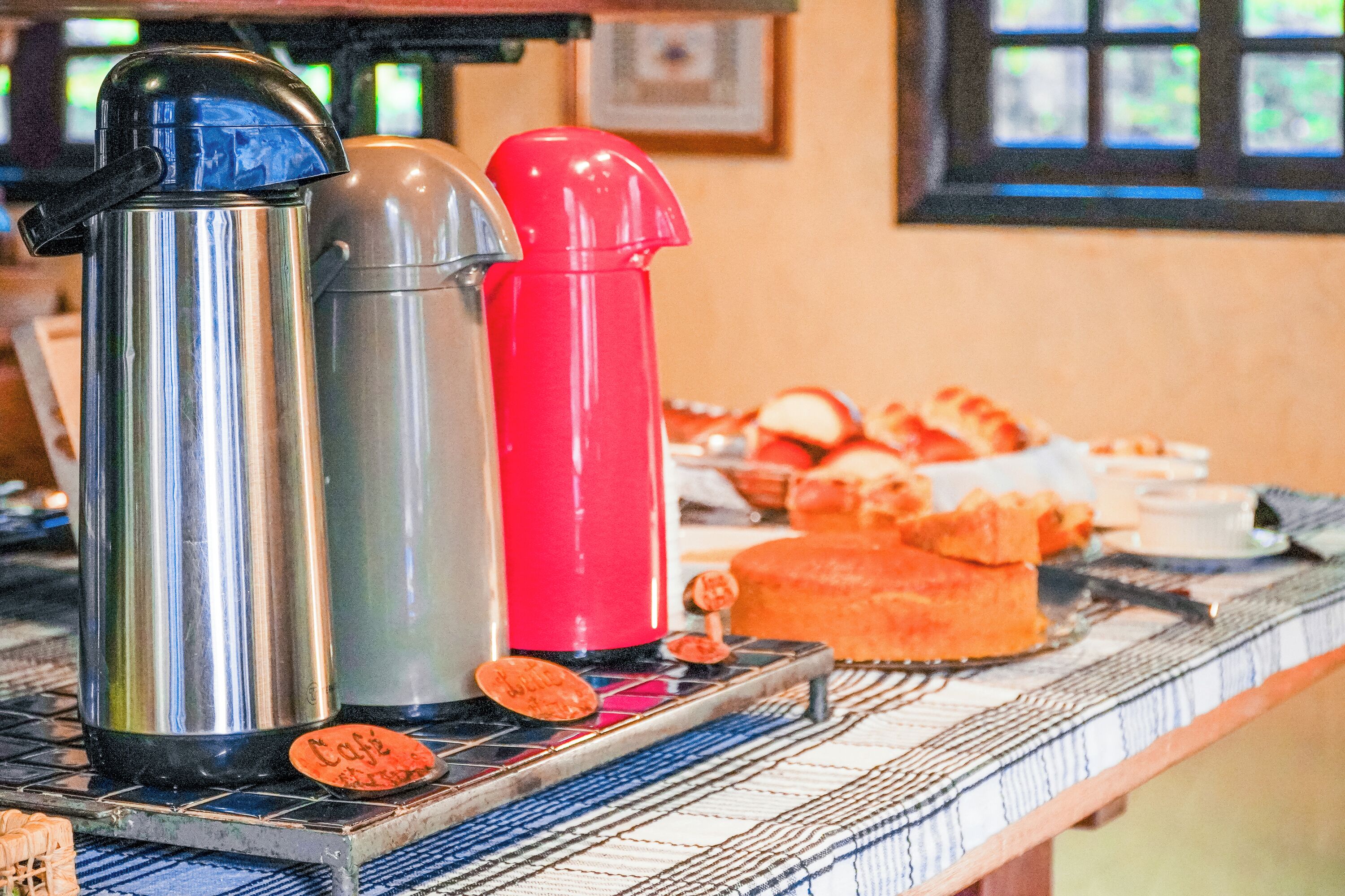 Una encimera de cocina con una cafetera de acero inoxidable, un dispensador de agua rojo y una bandeja de pasteles.