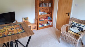 A room with a wooden bookshelf, a television, a board game, a wicker chair, and a door.