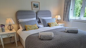 A neatly made double bed with a grey quilt, two bedside tables with lamps, and a window with curtains.