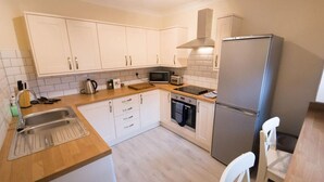 Een kleine keuken met witte kastjes, een roestvrijstalen spoelbak, een magnetron, een broodrooster en een koelkast.