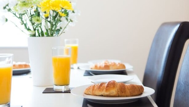 Een ontbijttafel met croissants, sinaasappelsap en een bloevas.