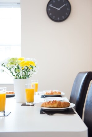 A breakfast table with croissants, orange juice, and a vase of flowers.