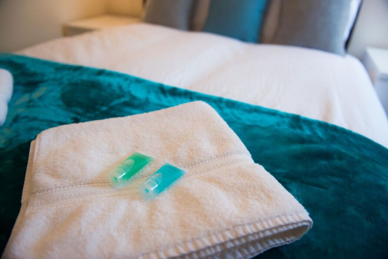A neatly folded towel with two green toiletries on a bed with a teal bedspread.