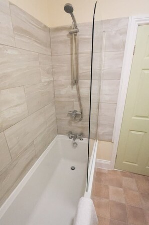 Ducha con cabezal de ducha manual y grifo empotrado, bañera y retrete.