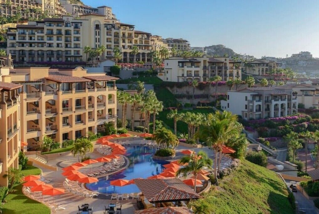 Ein Resort mit mehreren Gebäuden, einem zentralen Poolbereich mit Sonnenschirmen und umgebender Bepflanzung.