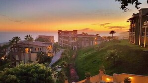 Un hôtel situé sur la côte, composé de plusieurs bâtiments, doté d’un sentier et offrant une vue sur l’océan au coucher du soleil.