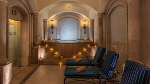 Un espace spa avec des murs en pierre, un mur décoré de mosaïques et deux fauteuils de relaxation.